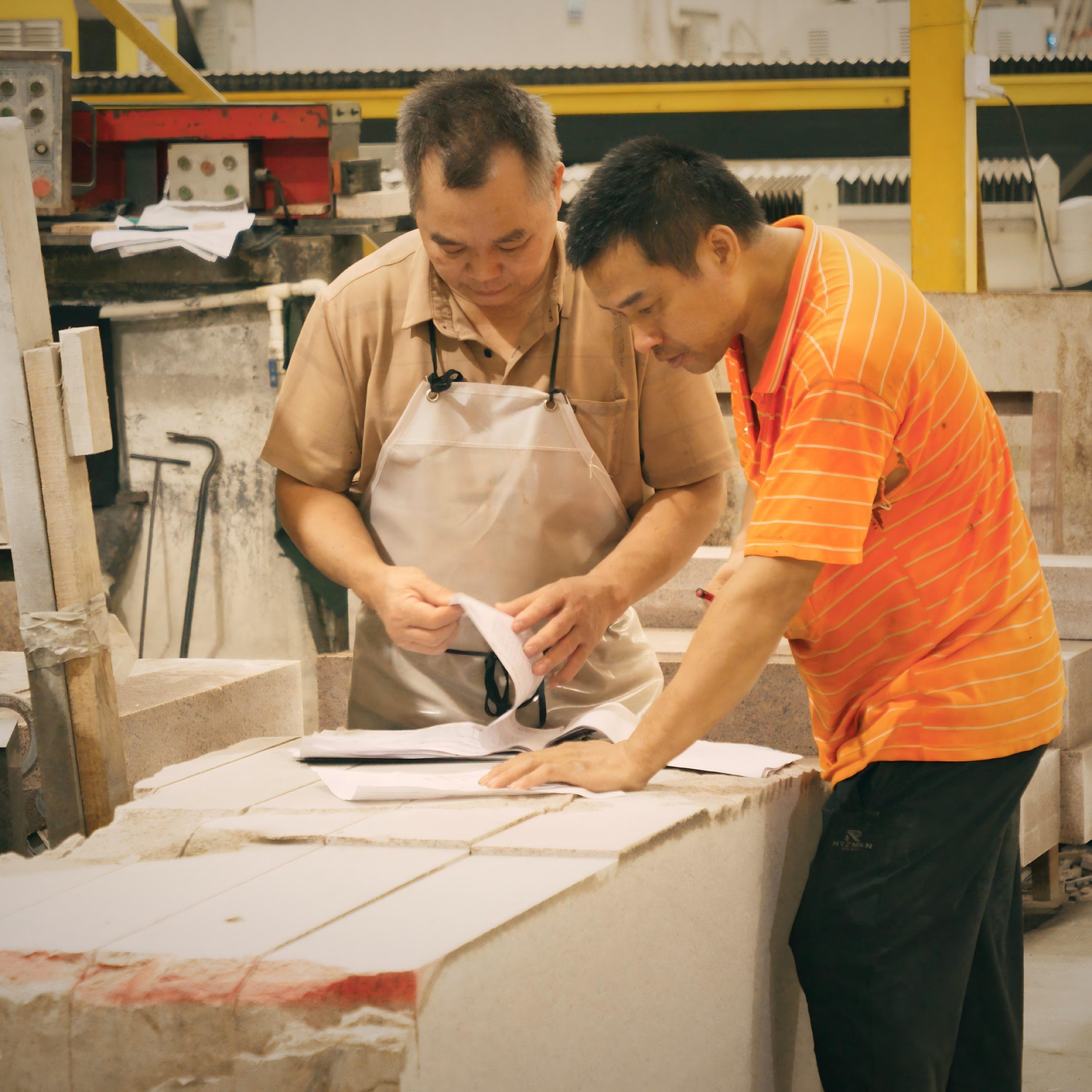 Skilled workers inspecting designs and blueprints during handcrafted stone processing in a factory